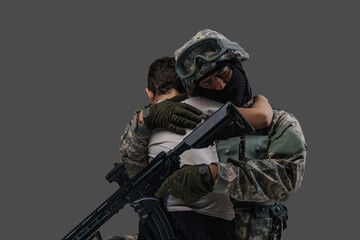 Portrait of professional serviceman dressed in camouflage clothes hugging little boy.