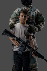 Shot of brave soldier and little child holding rifle isolated on gray background.