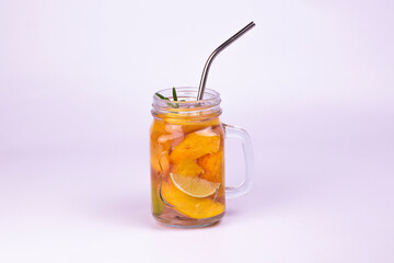 Glass of juice with peach slices, rosemary and straws on white background. Refreshing summer drinks.