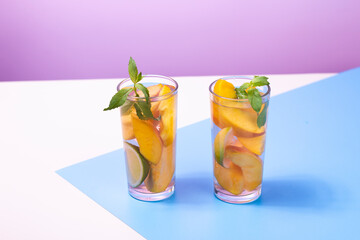 Refreshing summer drink. Peach juice or cocktail with peach slice, ice cube and mint on abstract geometrical white, blue and pink background.