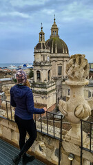 A woman standing on the platform of the Church of the Badia di Sant?Agata in Catania, Italy, Sicily, Europe. Panoramic view on the the city on a cloudy overcast day. Tourism, sight seeing