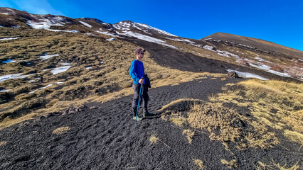 Man surrounded by golden grass hiking on volcanic landscape of volcano mount Etna, in Sicily,...