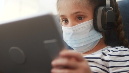 distance learning online lessons. child girl with digital tablet in mask studying remotely at home. education coronavirus online lessons lockdown concept. child learns distance learning school