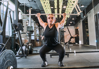 Sporty girl squats with barbell during training at the empty gym