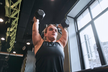 Low angle view of the midget woman lifting the dumbbells - obrazy, fototapety, plakaty