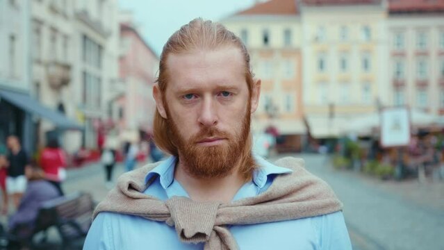 Attractive redhead bearded man with long hair standing on the street looking confident at camera. Businessman. Hipster. Caucasian people. Business portrait.