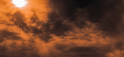 Dramatic stormy sky in orange tones, with the sun and rays breaking through. Selective focus.