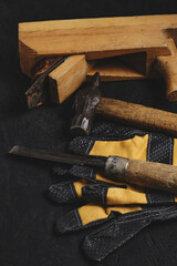 Set of tools for carpenters, hammer, chisel and plane with gloves dark wooden background.