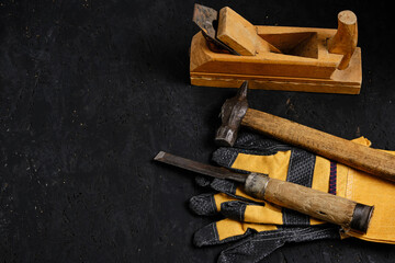 Set of tools for carpenters, hammer, chisel and plane with gloves dark wooden background.