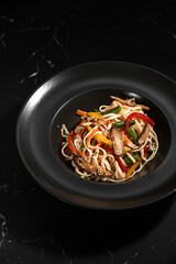 Japanese udon noodles fried in a wok. Udon noodles with vegetables on a dark background.