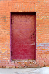 The old door is inhabited by tinplate and painted in burgundy color in a brick wall