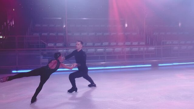Pair of figure skaters in black stage costumes perform death spiral element,partner releases woman,they skate in synchronous parallel step movements.Slow motion.Concept of pair skating,ice dancing