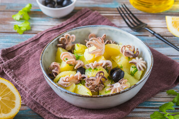 Potato salad with small octopuses and olives in a gray bowl on a wooden background. Recipes for potato salads.