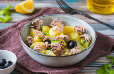 Potato salad with small octopuses and olives in a gray bowl on a wooden background. Recipes for...