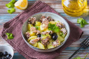 Potato salad with small octopuses and olives in a gray bowl on a wooden background. Recipes for potato salads.