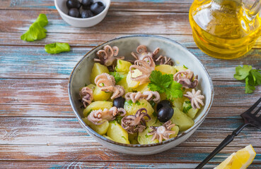 Potato salad with small octopuses and olives in a gray bowl on a wooden background. Recipes for potato salads.