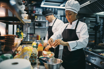 Black female chef cracking an egg while preparing food in restaurant.