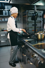 Happy African American female chef preparing food in restaurant.