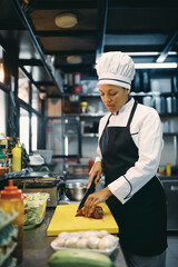 Black female chef chopping food while preparing meal at restaurant kitchen.