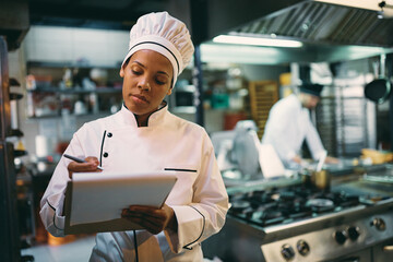 Black female chef going through checklist while working in kitchen at restaurant.