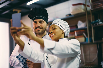 Fototapeta premium Happy cooks taking selfie while working at restaurant kitchen.