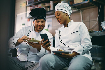 Happy chefs using smart phone on break in kitchen at restaurant.