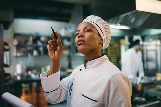 Black female chef examining stock of groceries at restaurant kitchen.