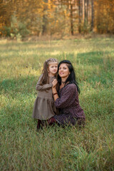 Fototapeta premium mother and daughter are hugging and smiling, sitting on the grass in the park