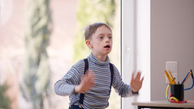 Hyperactive autistic boy jumping gesturing indoors laughing having fun. Portrait of cheerful happy Caucasian child with mental disorder enjoying leisure smiling. Autism and childhood concept