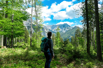 Woman with backpack standing on rock on a hiking trail in early spring with panoramic view on the mountain peaks of Hochschwab Region in Upper Styria, Austria. Forest in Alps, Europe. Karlhochkogel