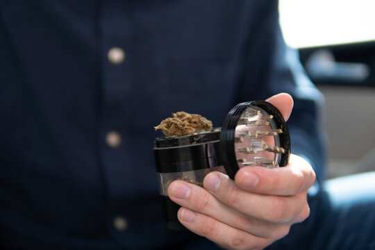 grinder and shredded cannabis joint packet of weed on a car background close up