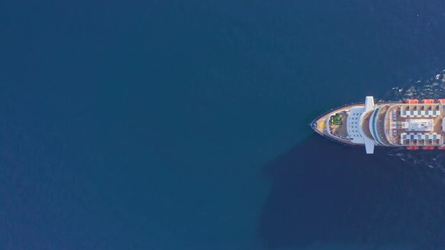 Aerial: large luxury cruise ship at sea. Big passenger ocean liner with pool on deck sailing in deep blue water top down view. Maritime travel across ocean tourism vacation holidays concept.