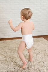 small child in a disposable diaper against a white wall - view from the back
