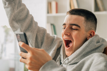 young teenager at home excited with mobile phone celebrating