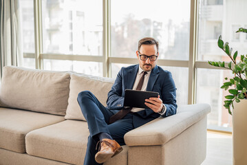 Confident businessman using digital tablet while sitting on sofa at office