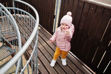 Baby girl show lolipop on wooden observation tower.