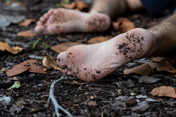 A man without shoes is lying on the ground. Feet in the ground. Possible murder in the forest. Soft focus
