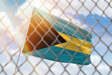 A steel mesh against the background of a blue sky and a flagpole with the flag of bahamas