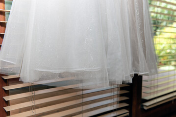 Obraz na płótnie Canvas Bride's wedding dress hanging in the sunlight, highlights the sheer hem of the skirt portion on the bottom