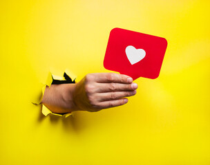 Man hold social media like, demonstrates approval or agreement through torn paper wall yellow...