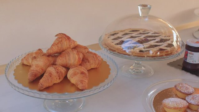 Served table with pastries during breakfast in the buffet. A hand removes a glass dome from a plate with croissants. 08.10.2021 Borgagne, Puglia, Italy. 