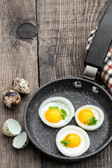 Fried quail eggs in onion ring in frying pan on wooden table