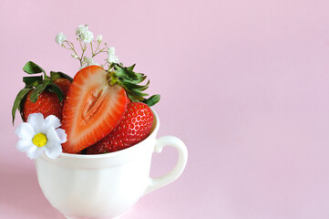 Ripe strawberries in a ceramic mug with flowers. Selective focus with copy space on pink background