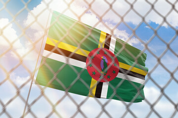 A steel mesh against the background of a blue sky and a flagpole with the flag of dominica