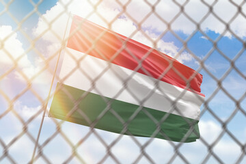 A steel mesh against the background of a blue sky and a flagpole with the flag of hungary