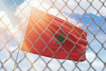 A steel mesh against the background of a blue sky and a flagpole with the flag of morocco