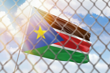 A steel mesh against the background of a blue sky and a flagpole with the flag of south sudan