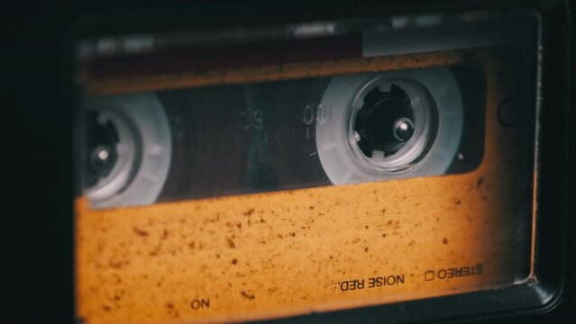 Vintage yellow audio cassette playing in a deck of an old tape recorder. Audiocassette with blank label in retro player spinning. Close-up. Call recording, retro playback, reel with tape rotating