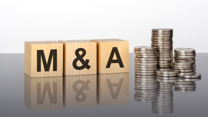 ma - text on wooden cubes on a cold grey light background with stacks coins