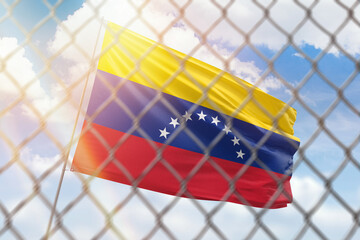 A steel mesh against the background of a blue sky and a flagpole with the flag of venezuela